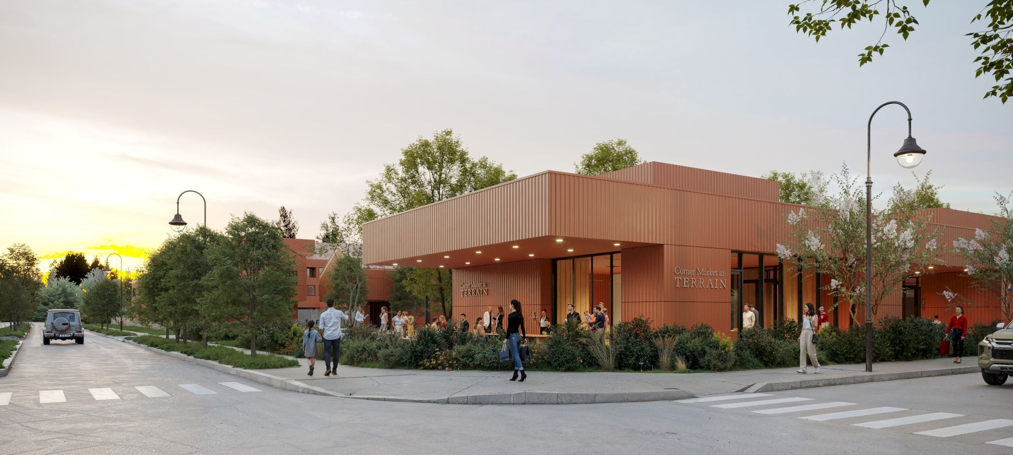 The image shows a modern brick building surrounded by trees and streetlights, with people walking nearby on a sunny day.